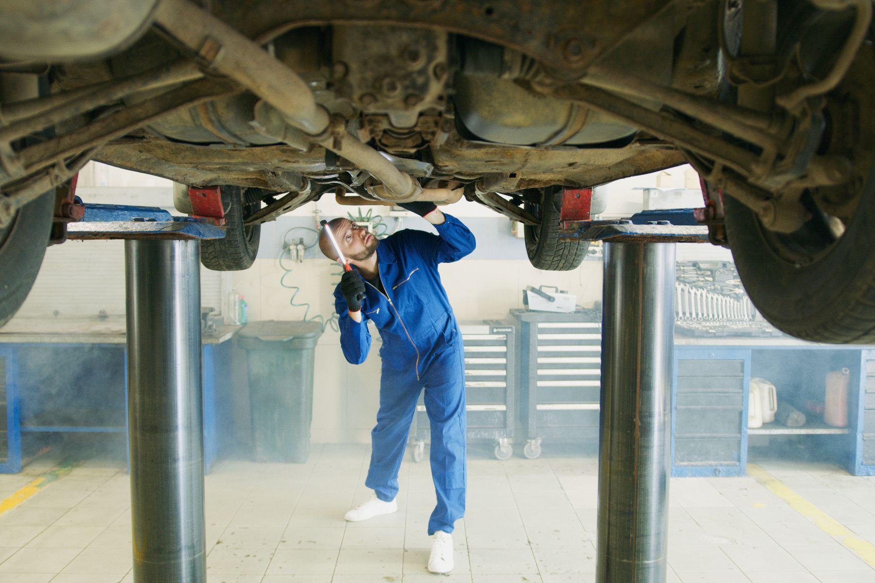 A mechanic inspects a vehicle from beneath a service lift.